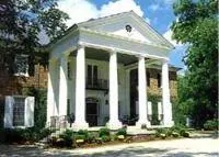 A large white building with columns and bushes.